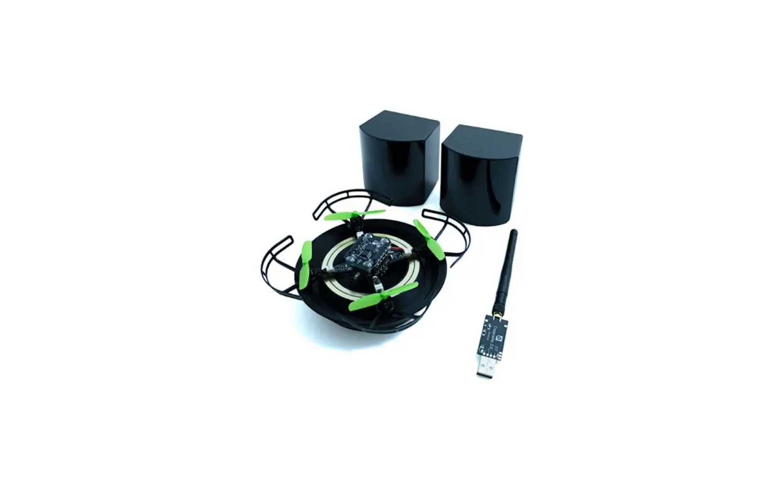 Crazyflie 2.1 Brushless nano quadcopter with green propellers and a black protective cage, resting on a circular wireless charging pad, with two black charging blocks behind it and a USB radio dongle with an antenna beside it, on a white background.