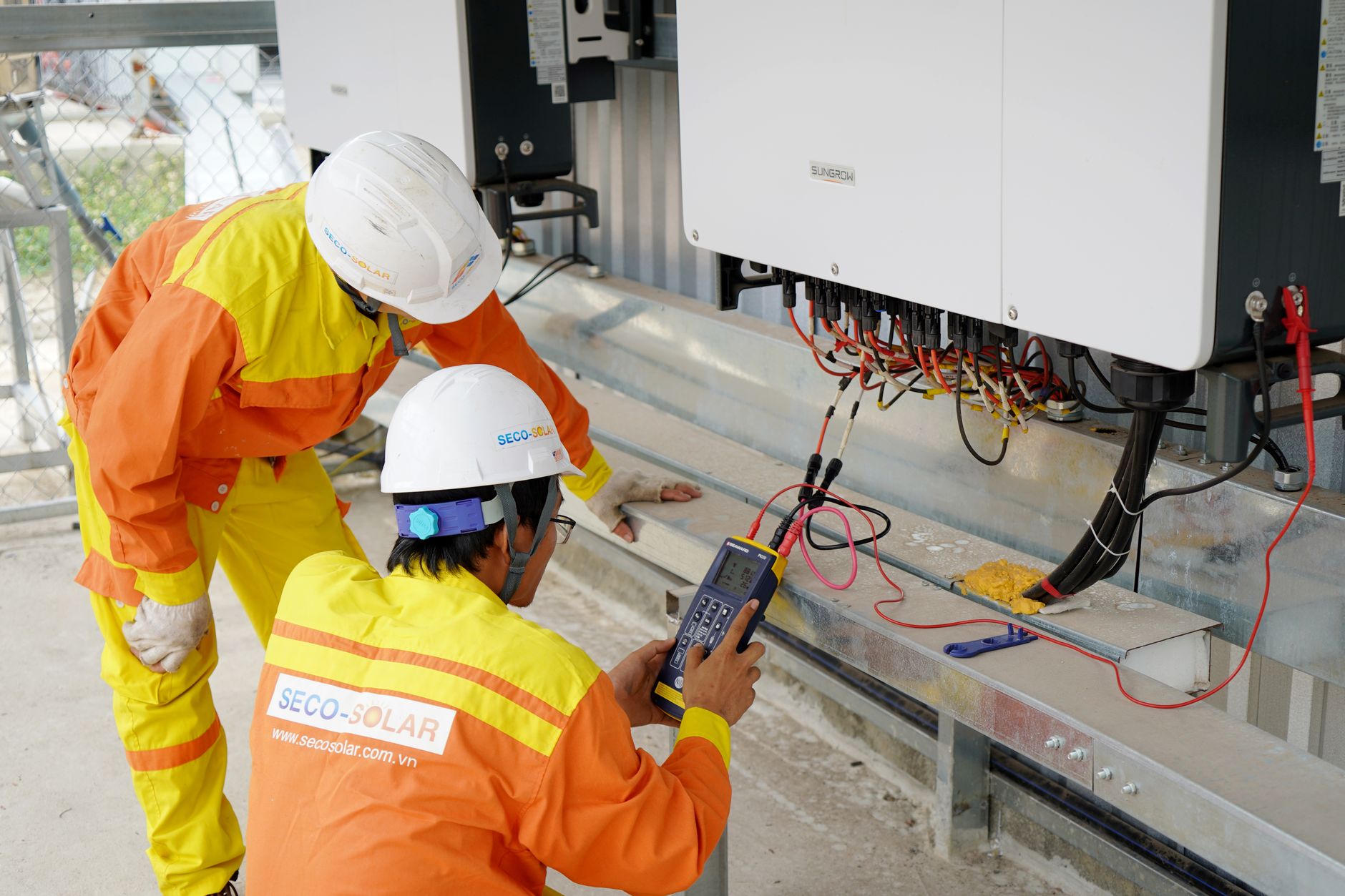 Demonstrating the efficiency testing of an ASIC miner. Two electrical engineers installing and testing solar power systems wearing safety gear at a construction site.