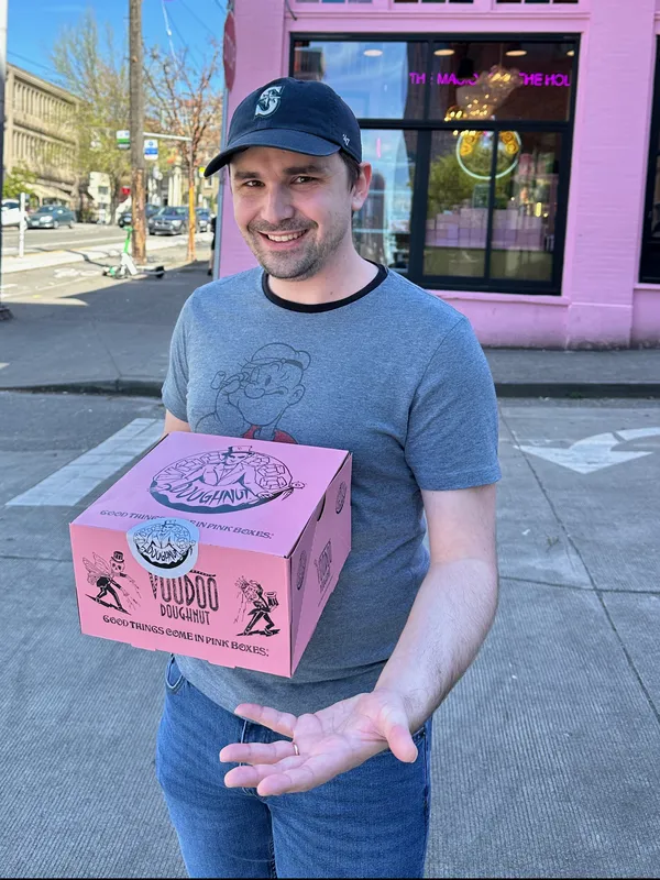Tyler McNamer today, smiling and holding a box of doughnuts