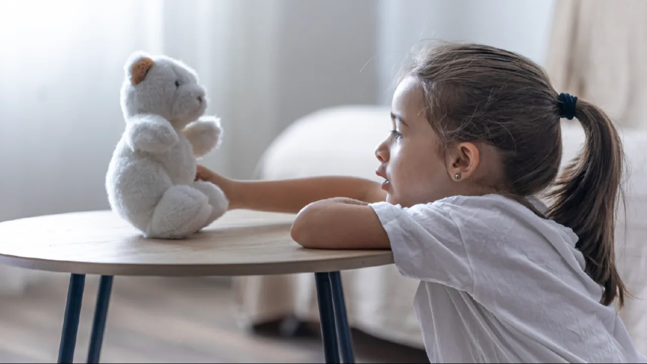 A little girl talking quietly to her teddy bear