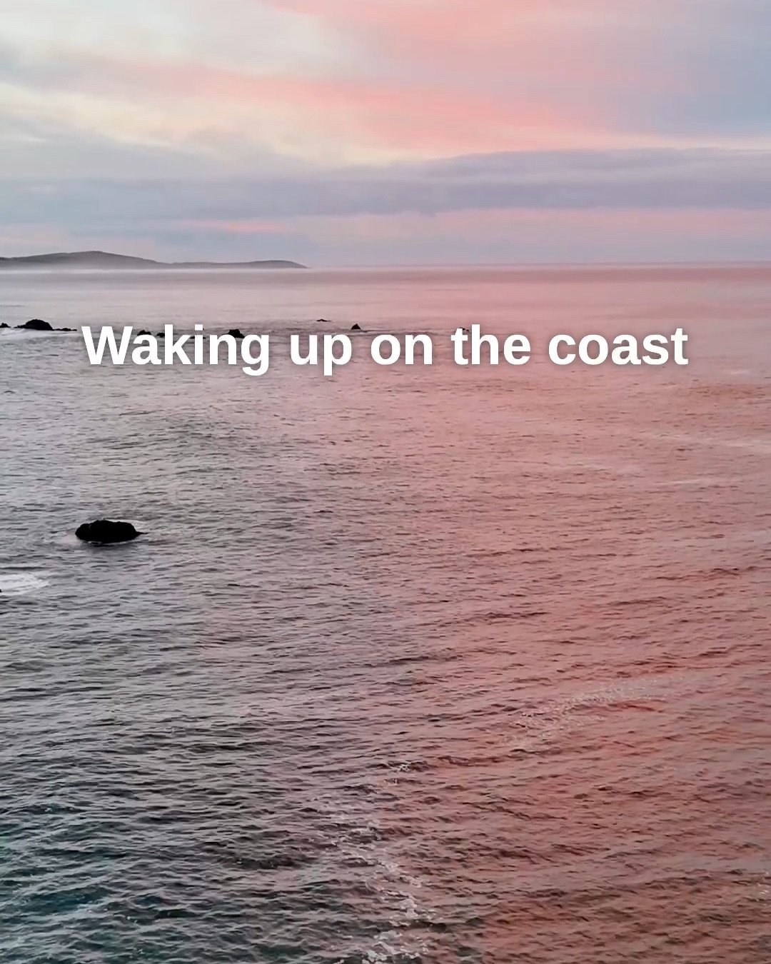 Pink sunrise light over the Pacific off Bodega Bay, with the words Waking up on the coast across the water.